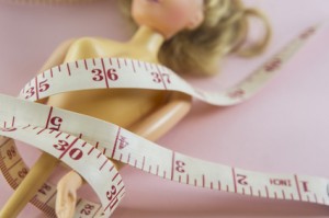 closeup measuring tape with women plastic doll on pink background
