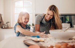Happy young girl with her mother making dough. Mother and daughter baking in kitchen.
