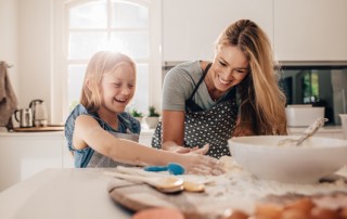 Happy young girl with her mother making dough. Mother and daughter baking in kitchen.